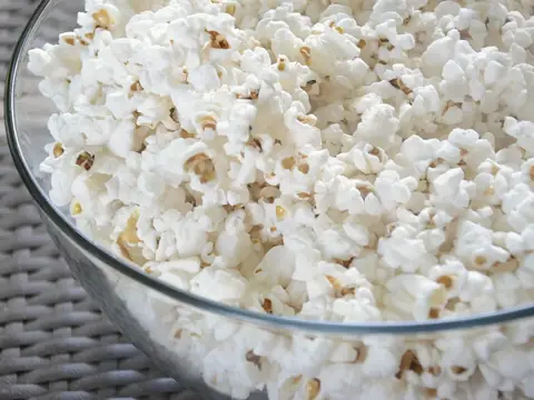 Bol en verre rempli de pop-corn, posé sur une table tressée
